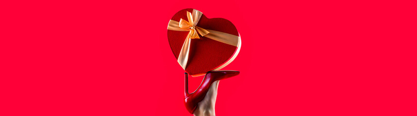 Female legs wearing high heels. Gift in heart shape on the background. Gift tied with ribbon....