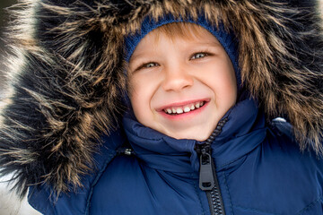 Boy wearing a fur hooded winter coat. Close up portrait of cute happy smiling child on a cold...