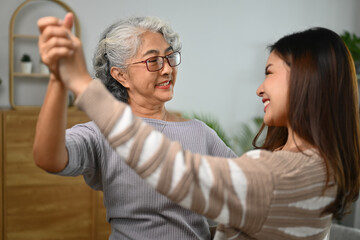 Happy gray haired middle age mother dancing with grown up daughter in living room