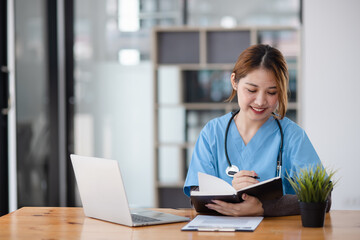 Asian female doctor working with a patient clipboard and digital laptop sitting at desk in...