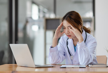 Asian female doctors face heavy levels of stress too with stethoscope sitting at desk in hospital,...