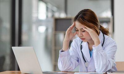 Asian female doctors face heavy levels of stress too with stethoscope sitting at desk in hospital,...