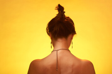 Beautiful thin woman from the back, with a chain around her neck on a yellow background