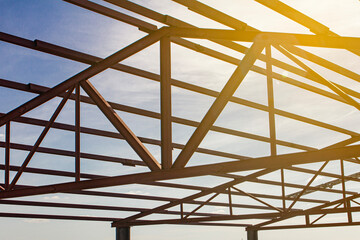 installation of hangar metal structures using a crane and installers, against the background of a blue sky - obrazy, fototapety, plakaty
