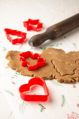 Top view of gingerbread cookie dough with red Christmas molds, heart, doll and star, on white paper with rolling pin, vertical