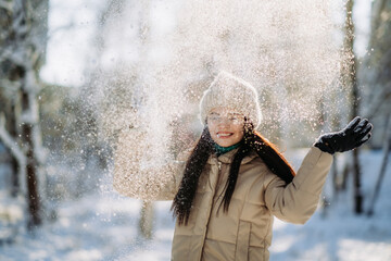 Portrait of a beautiful girl in winter clothes standing in a winter park on a sunny day and smiling. The winter vacation. Copy space.