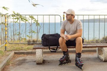 Portrait of happy handsome male roller in inline roller skates sitting on bench on the park.