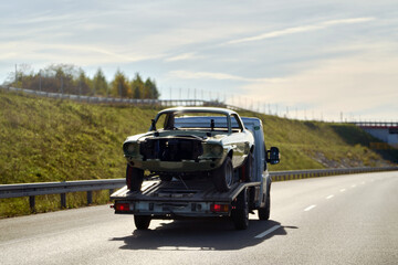 Fototapeta na wymiar Recover a Retro Car After an Accident. A Project to Restore a Classic Car with the Help of a Tow Truck. A Vintage Car Damaged by a Collision on the Highway.