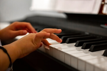 Obraz premium The girl playing the piano, close-up piano, white and black keyboard. Close-up portrait girl playing a melody on the keys of an electronic synthesizer in the living room.