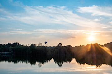 Captured at the moment when dawn breaks, this image presents a serene lake reflecting the awakening sky. The sun crests the horizon, scattering radiant beams and awakening the world with soft light. A