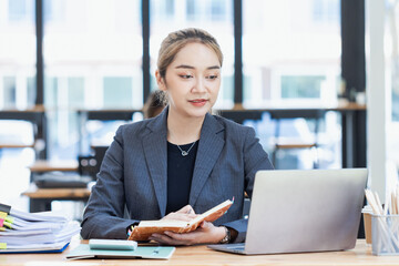 Asian businesswoman working on laptop and financial document paper sitting at desk in office...