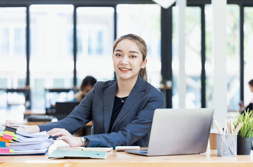 Asian businesswoman working on laptop and financial document paper sitting at desk in office workplace.