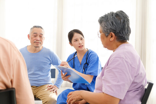 The caregiver therapist sits with a group of Asian senior people in a circle for checking physical and mental health in a group elderly therapy session. The nursing home concept. Vertical image.