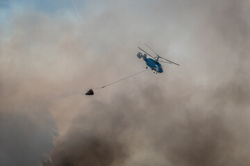 Helicóptero rodeado de fumo a descarregar a água do balde sobre um incêndio florestal