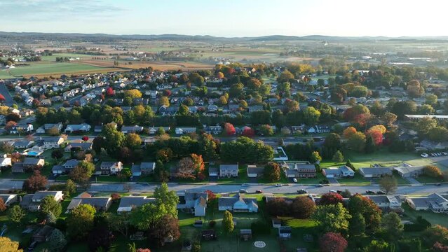 American neighborhood during autumn. Wide aerial truck shot featuring suburb housing development with many houses and homes. Farmland in background.