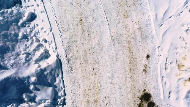 Snow-Covered Winding Road Neighborhood or Long Driveway with Tire Tracks and Mud Streaks Packed in with Footprints. Aerial Drone Top-Down View of Dangerous Road Conditions