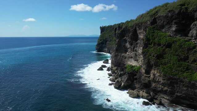 The cliffs of Uluwatu, Bali on a hot summers day with waves crashing against the rocks, aerial.