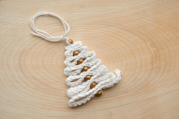 Obraz na płótnie Canvas Knitted Christmas Tree as a Gift. Cool Toy Tree Made of Threads on a Wooden Pattern. Miniature Decoration. Handmade Nordic Holiday Decor. Scandinavian Style Design. DIY. Minimal Ornament. Zero Waste