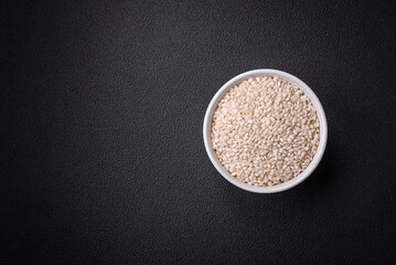 White uncooked rice in a round ceramic bowl on a dark concrete background