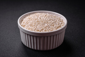 White uncooked rice in a round ceramic bowl on a dark concrete background