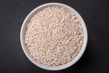 White uncooked rice in a round ceramic bowl on a dark concrete background