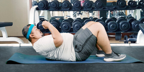 Overweight Asian guy doing some abs exercises in a weight room gym