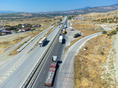 Top view of an asphalt road with trucks, fields, mountains near the town on a sunny day, Turkey.