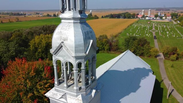 Drone shot strafing over a community chapel, showing the church bells, churchyard, and the surrounding farms, located in Montreal, Quebec in Canada.