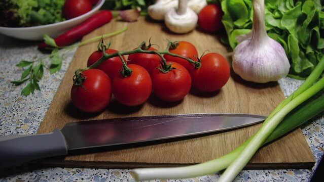  Background close-up of cherry tomatoes lying on a board next to a knife, onion, champignons, garlic and lettuce