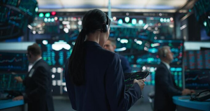 Successful Stock Exchange Manager Wearing Headphones, Working in Modern Office. Proactive Female Trader Browsing Financial Reports on a Tablet Computer, Using Software with Stock Market Auctions