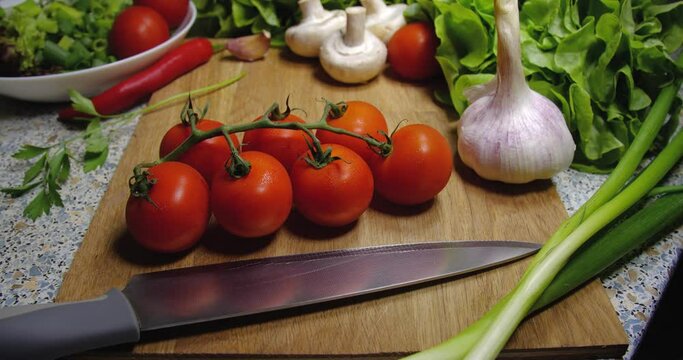  Background close-up of cherry tomatoes lying on a board next to a knife, onion, champignons, garlic and lettuce