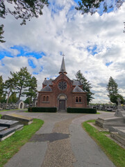 Fototapeta na wymiar This broader view of the Mechelen Cemetery chapel encompasses the somber yet peaceful surroundings where headstones and monuments stand in quiet companionship. The chapel, with its Gothic features and