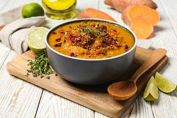 Sweet potato puree in bowl, spoon and ingredients on kitchen board on wooden background, close up