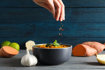Sweet potato puree in bowl, vegetables, hand and spices on wooden background