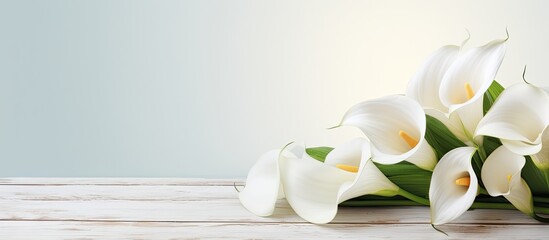 White calla flowers on a white wooden table, with room to write. - obrazy, fototapety, plakaty