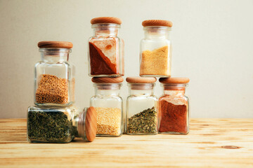 A group of seasonings in glass jars on a light wooden background. Paprika, herbs, mustard, garlic, front view, selective focus