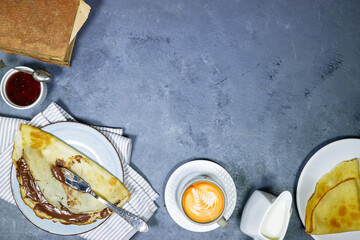 morning breakfast concept : Crepes stuffed with chocolate spread on blue plate with fig jam bowl and late art coffee, beans and old book