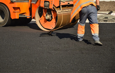 a worker levels the asphalt in front of a road roller