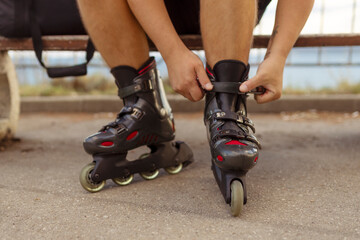 Legs of young man putting on roller skates in the park