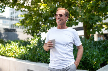 Fototapeta premium Man in white shirt and sunglasses drinking coffee in city park.
