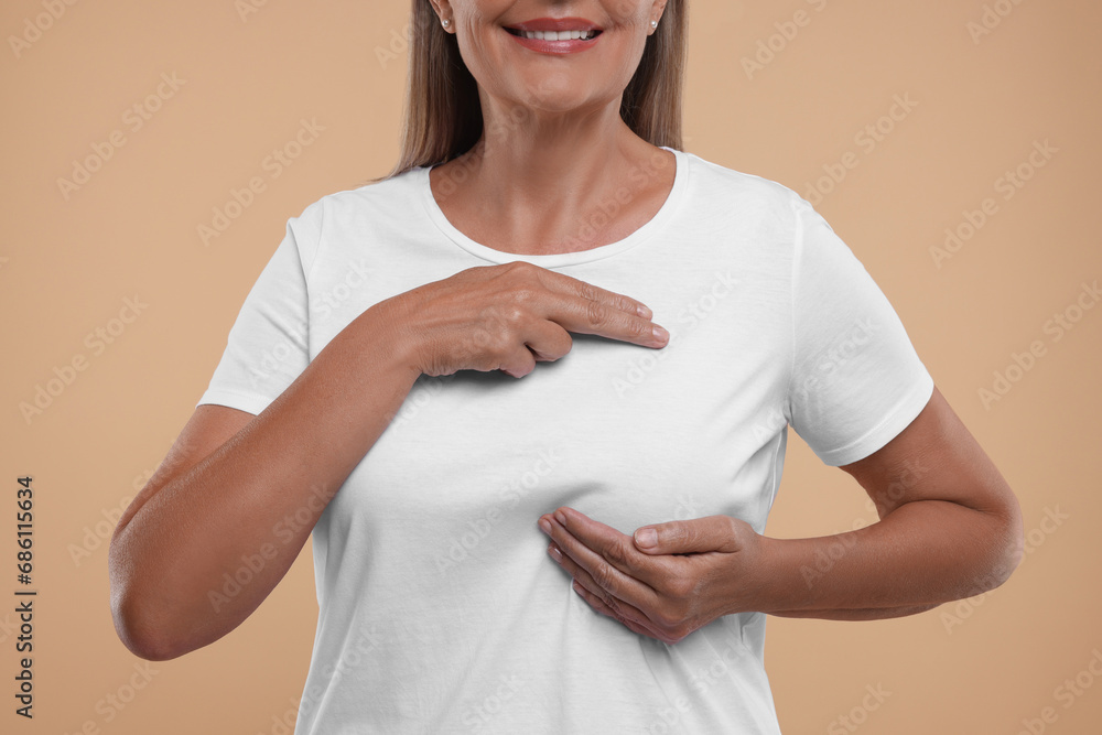 Wall mural Woman doing breast self-examination on light brown background, closeup