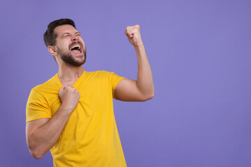 Fototapeta premium Emotional sports fan celebrating on purple background. Space for text