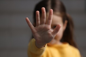 Child abuse. Little girl doing stop gesture on gray background, selective focus