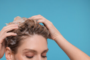 Woman washing hair on light blue background, closeup. Space for text