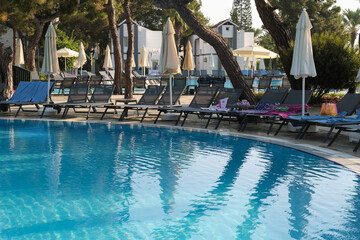 tranquil pool reflects the quiet of an early morning, sunbeds untouched by guests. Capturing the...