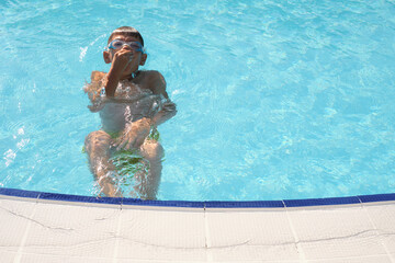 Child pauses in swimming, gripping the pool's edge tightly. Suits content on youth sports and the...