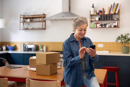 Senior female businesswoman packing orders and using a smartphone working from home