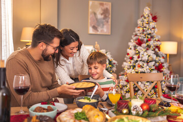 Mother and father offering apple pie to son during Christmas dinner at home