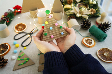 Close-up of Childrens Hands Holding a Christmas Tree Made of Cardboard Decorated With Colorful Balls. zero waste concept