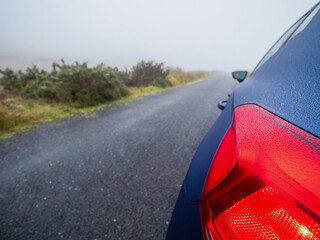 Blue small car parked on a small narrow country road during fog. Dangerous driving conditions due...